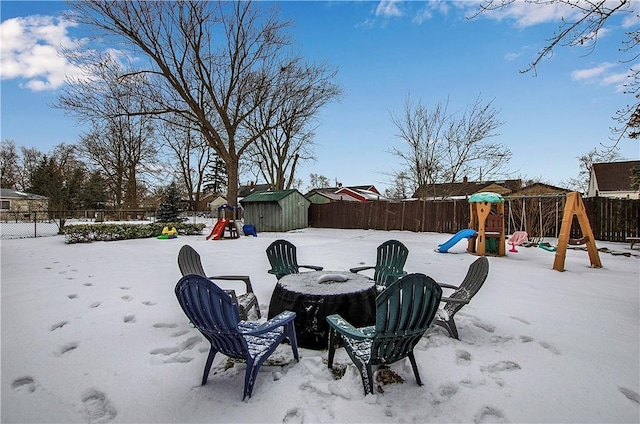 snow covered patio with a fire pit, a playground, and a storage unit