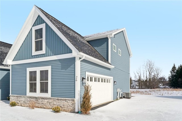 view of snowy exterior with a garage and central air condition unit