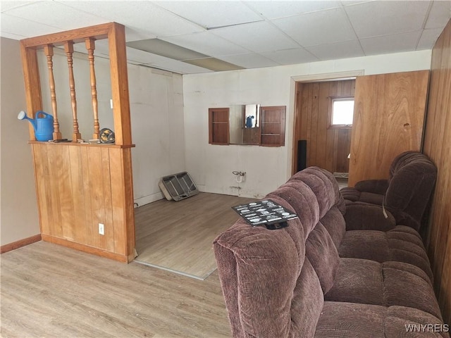 living room featuring a drop ceiling, light hardwood / wood-style floors, and wood walls