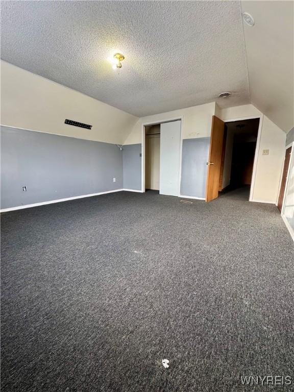 bonus room featuring dark colored carpet, lofted ceiling, and a textured ceiling