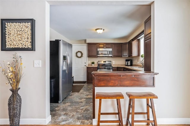 kitchen with a breakfast bar, sink, dark brown cabinets, kitchen peninsula, and stainless steel appliances