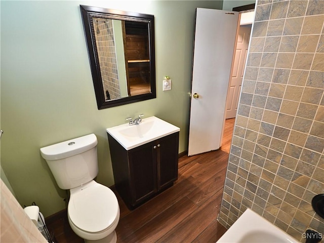 bathroom featuring hardwood / wood-style flooring, a tub to relax in, vanity, and toilet