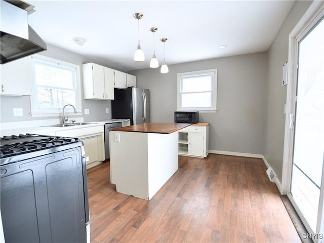 kitchen with stainless steel appliances, extractor fan, white cabinets, a kitchen island, and decorative light fixtures