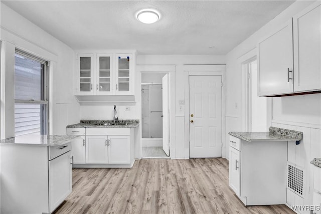 kitchen featuring sink, white cabinets, a textured ceiling, and light hardwood / wood-style flooring