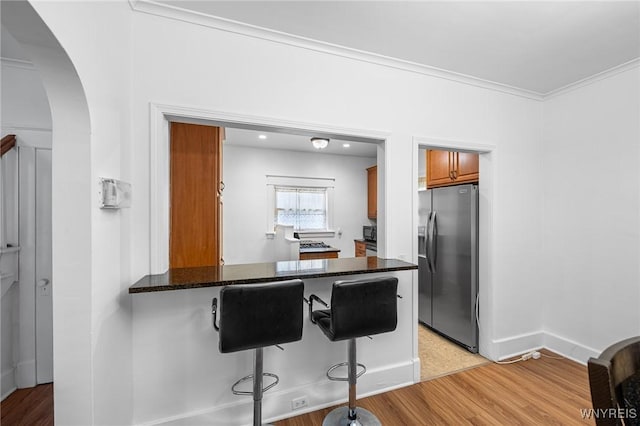 kitchen featuring stainless steel refrigerator with ice dispenser, ornamental molding, a kitchen breakfast bar, kitchen peninsula, and dark stone counters