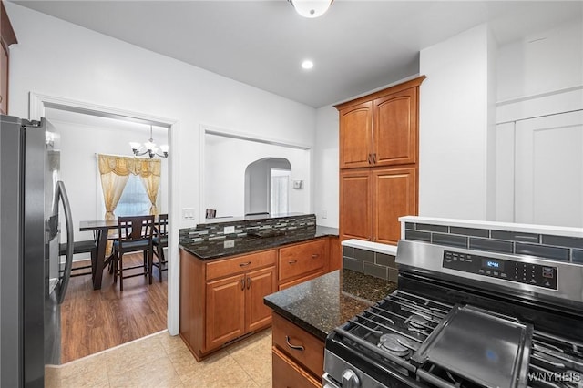 kitchen with stainless steel gas range, black fridge with ice dispenser, a chandelier, light tile patterned floors, and dark stone countertops