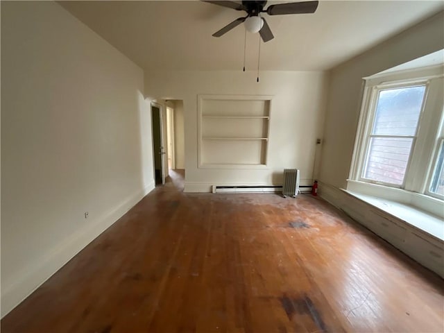 spare room featuring a baseboard heating unit, built in shelves, wood-type flooring, and ceiling fan