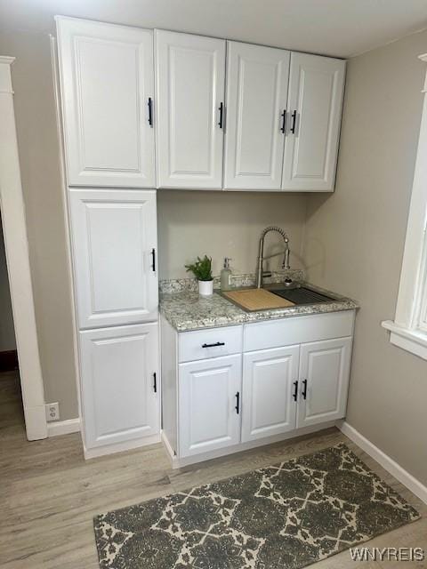 bar featuring light stone countertops, sink, white cabinets, and light hardwood / wood-style floors