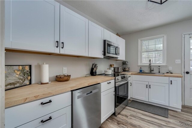 kitchen with appliances with stainless steel finishes, sink, white cabinets, and butcher block countertops