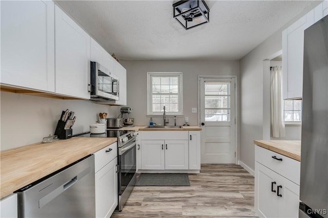 kitchen with sink, white cabinetry, a textured ceiling, light wood-type flooring, and stainless steel appliances