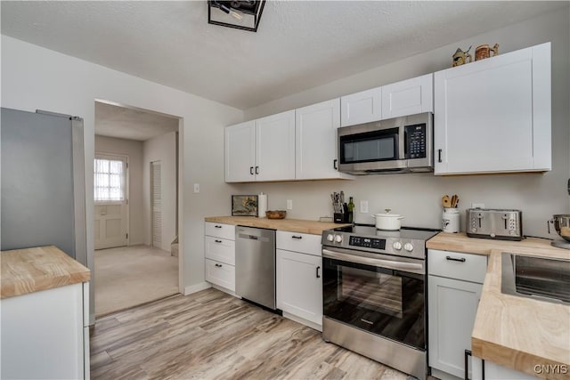 kitchen featuring wood counters, white cabinetry, a textured ceiling, stainless steel appliances, and light hardwood / wood-style floors