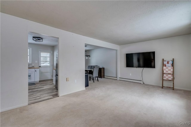 unfurnished living room with light carpet, a baseboard heating unit, and a textured ceiling