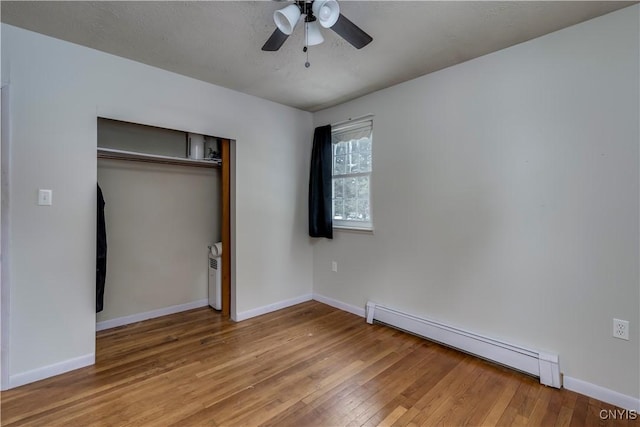 unfurnished bedroom featuring a baseboard heating unit, hardwood / wood-style floors, ceiling fan, and a closet