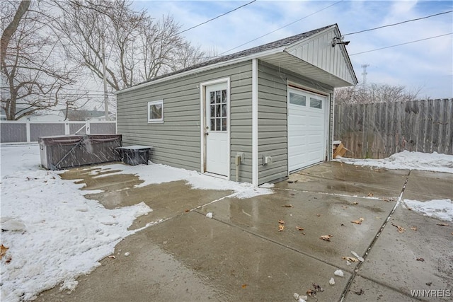 snow covered structure featuring a garage and a hot tub