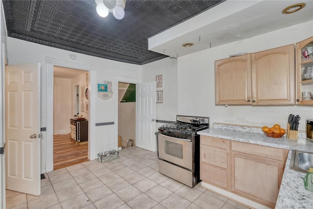 kitchen featuring gas range, light brown cabinets, light stone counters, and light tile patterned flooring