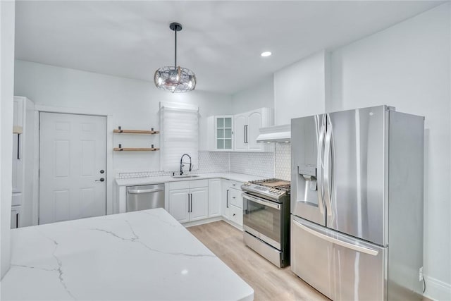 kitchen featuring appliances with stainless steel finishes, white cabinets, light stone counters, and decorative light fixtures