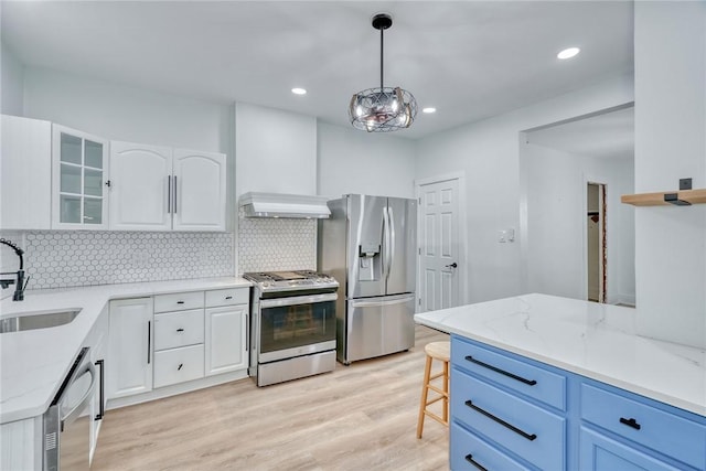 kitchen featuring wall chimney exhaust hood, sink, light stone counters, hanging light fixtures, and stainless steel appliances