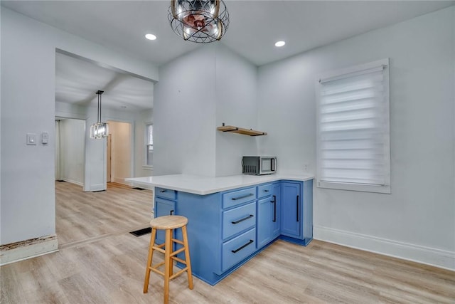 kitchen with a breakfast bar area, hanging light fixtures, blue cabinets, kitchen peninsula, and light wood-type flooring