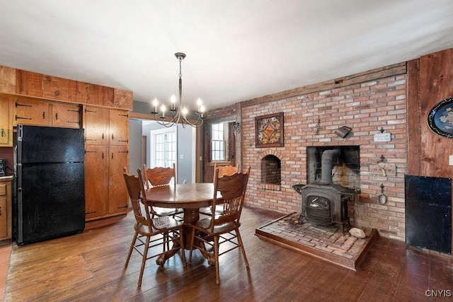 dining space featuring an inviting chandelier, brick wall, a wood stove, and hardwood / wood-style floors