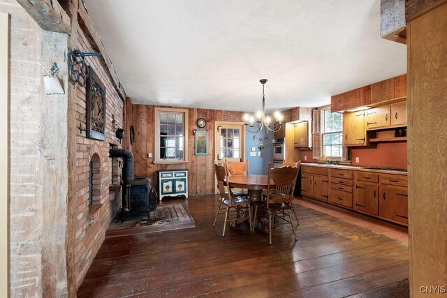 dining area with an inviting chandelier, a wood stove, dark wood-style flooring, and wooden walls