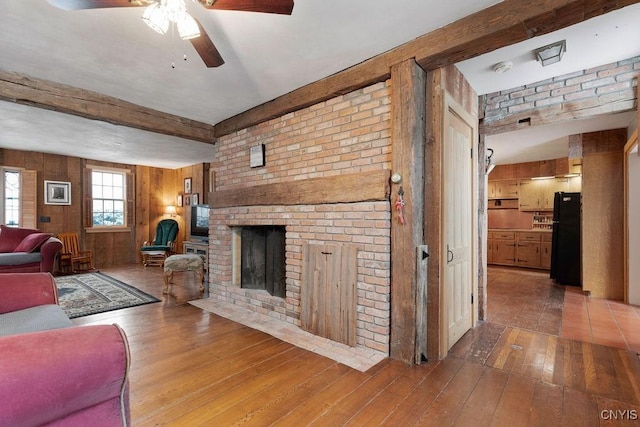living room with a fireplace, wood walls, hardwood / wood-style floors, a ceiling fan, and beamed ceiling