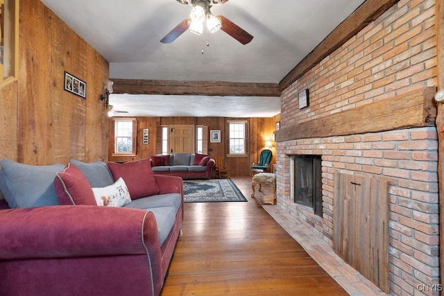 living room with hardwood / wood-style floors, wooden walls, a brick fireplace, and ceiling fan