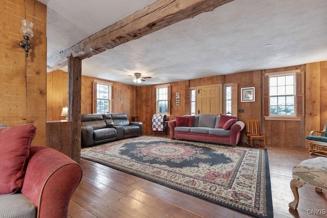 living room featuring ceiling fan, wood-type flooring, wooden walls, and beam ceiling