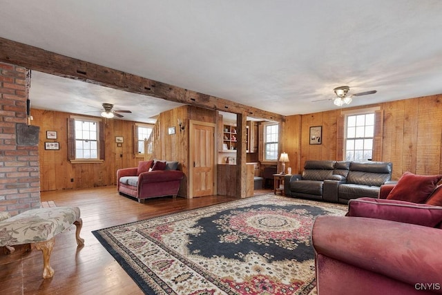 living room featuring ceiling fan, beam ceiling, hardwood / wood-style floors, and wood walls