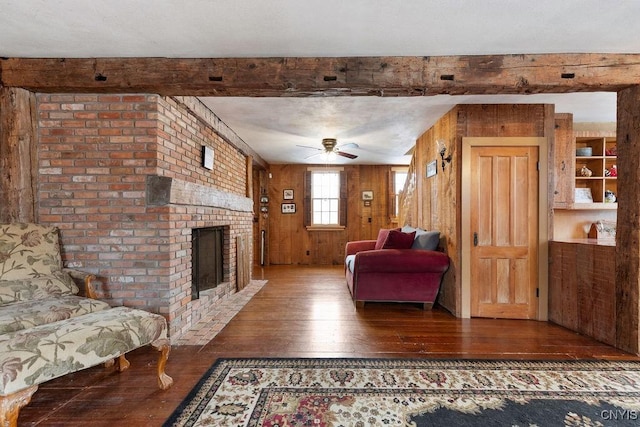 living room with wood-type flooring, wood walls, a brick fireplace, and ceiling fan