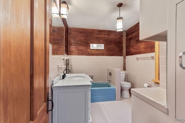 bathroom with vanity, wainscoting, toilet, tile walls, and a bathing tub