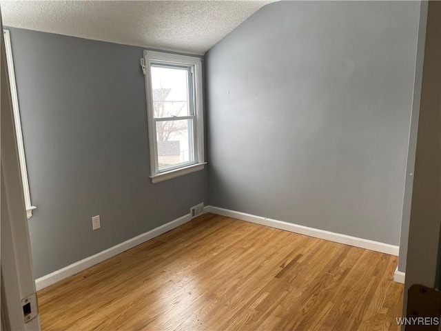 spare room with lofted ceiling, light wood-type flooring, and a textured ceiling