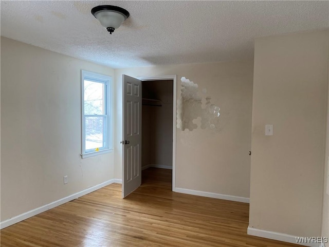 unfurnished bedroom featuring a walk in closet, a textured ceiling, light hardwood / wood-style floors, and a closet