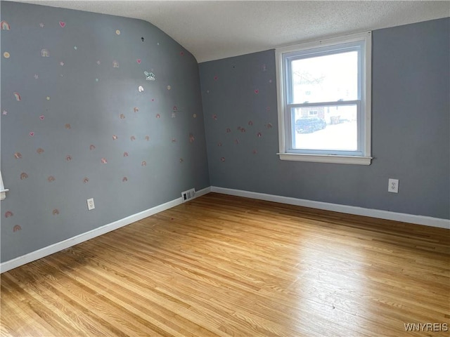 empty room featuring lofted ceiling, light hardwood / wood-style floors, and a textured ceiling