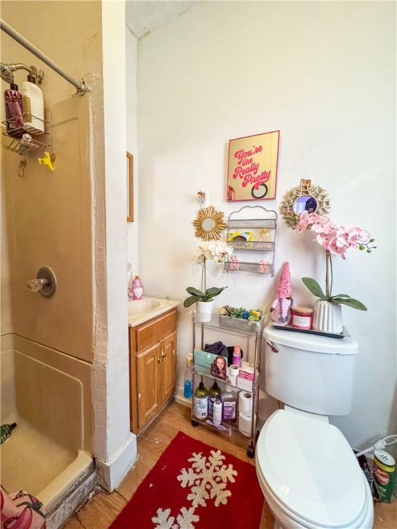 bathroom with hardwood / wood-style flooring, a shower, vanity, and toilet