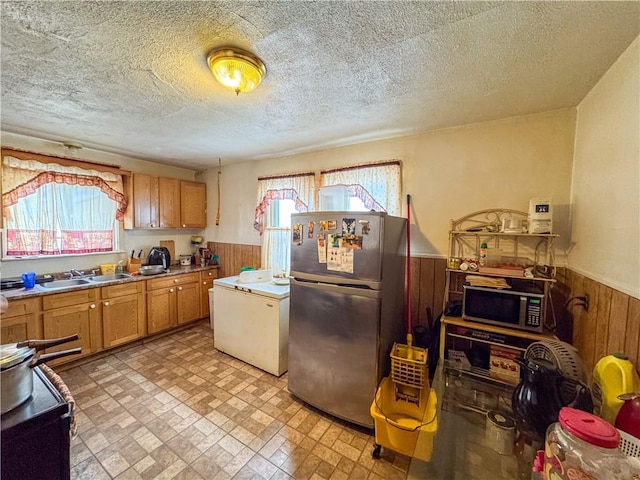 kitchen featuring stainless steel appliances, wooden walls, sink, and a textured ceiling