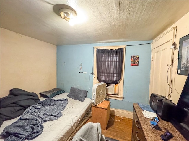 bedroom with cooling unit, wood-type flooring, and a textured ceiling