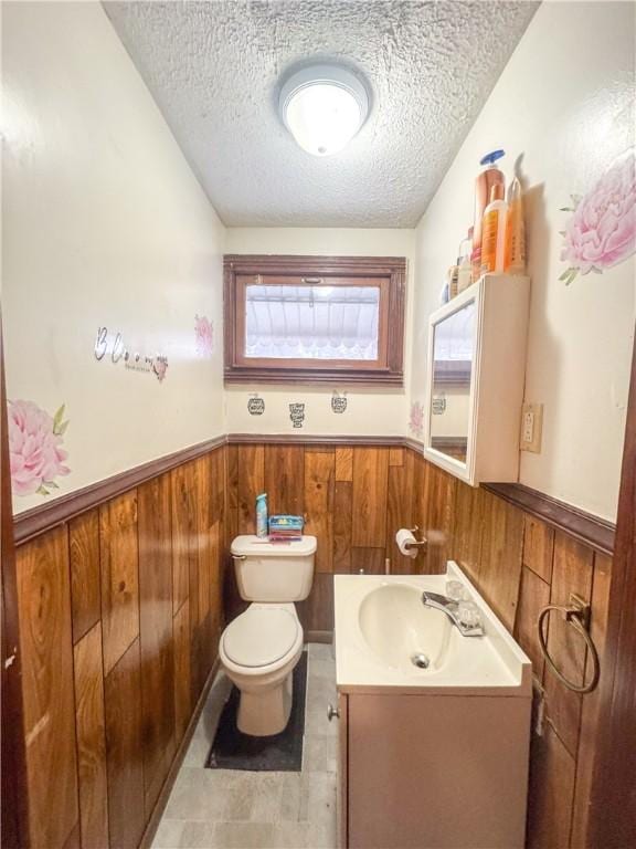 bathroom featuring vanity, a textured ceiling, wooden walls, and toilet