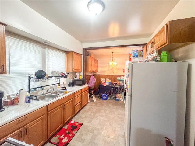 kitchen featuring sink, an inviting chandelier, hanging light fixtures, white refrigerator, and wooden walls