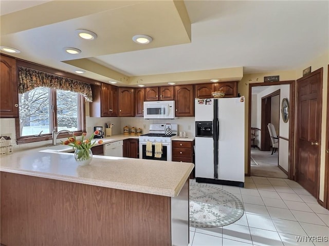 kitchen featuring light tile patterned floors, white appliances, kitchen peninsula, decorative backsplash, and a raised ceiling