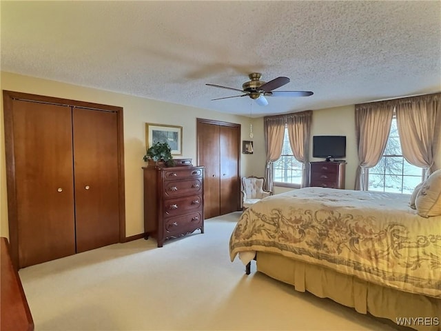 carpeted bedroom featuring ceiling fan, a textured ceiling, and two closets