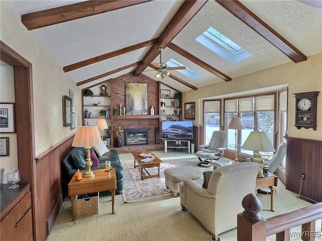 carpeted living room featuring lofted ceiling with skylight, a brick fireplace, a textured ceiling, wooden walls, and ceiling fan