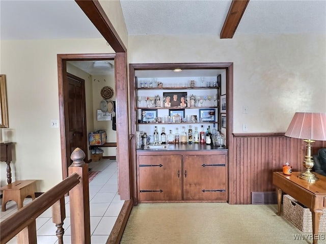 bar with beamed ceiling, wood walls, a textured ceiling, and light tile patterned floors