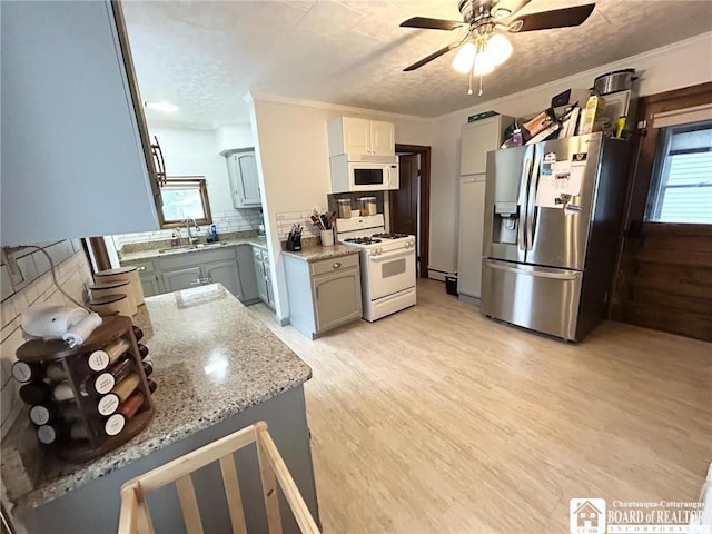 kitchen with sink, ornamental molding, light stone counters, light hardwood / wood-style floors, and white appliances