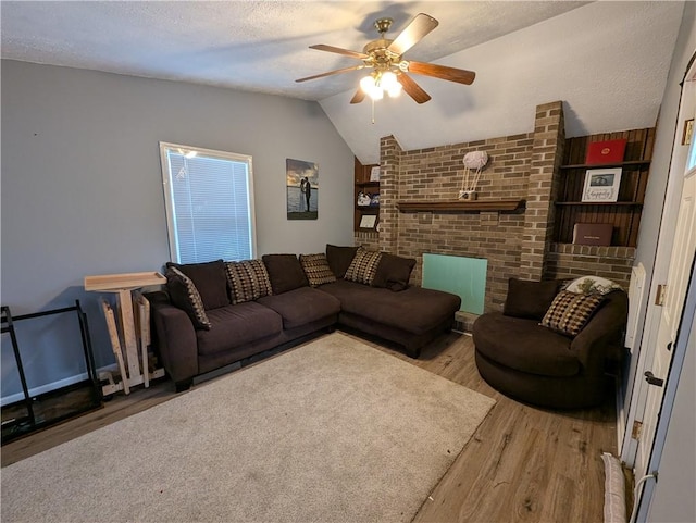 living room featuring lofted ceiling, ceiling fan, a textured ceiling, a brick fireplace, and light wood-type flooring