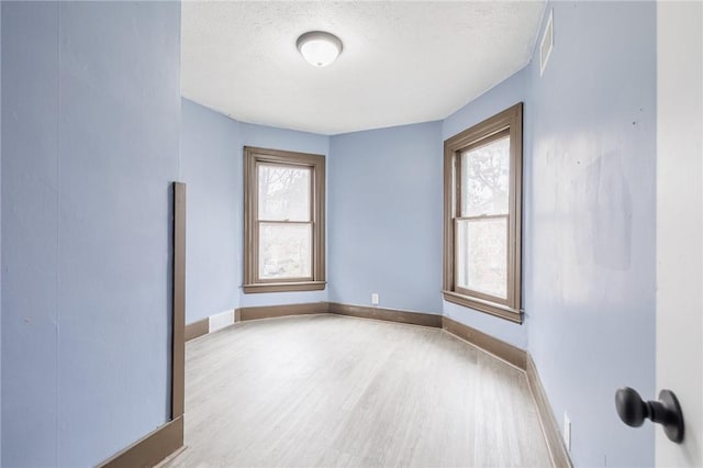 unfurnished room with light wood-type flooring and a textured ceiling