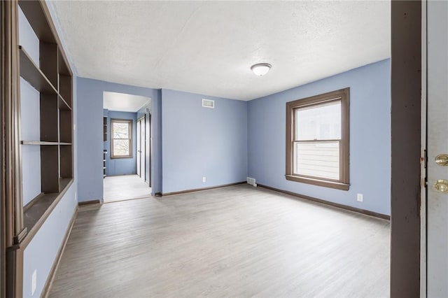 unfurnished room with a textured ceiling and light wood-type flooring