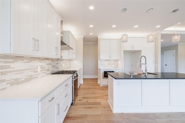 kitchen with a kitchen island with sink, hanging light fixtures, stainless steel range with gas stovetop, and white cabinets