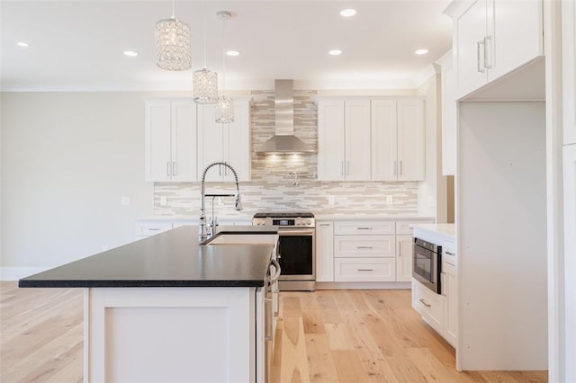 kitchen featuring white cabinetry, gas stove, a kitchen island with sink, and wall chimney range hood