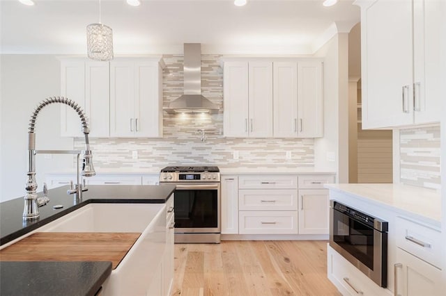 kitchen featuring white cabinetry, pendant lighting, stainless steel appliances, and wall chimney exhaust hood