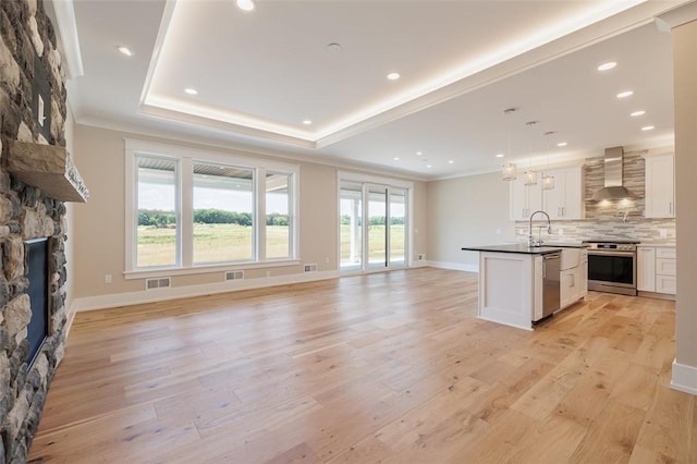 kitchen featuring stainless steel appliances, wall chimney range hood, white cabinets, and decorative light fixtures